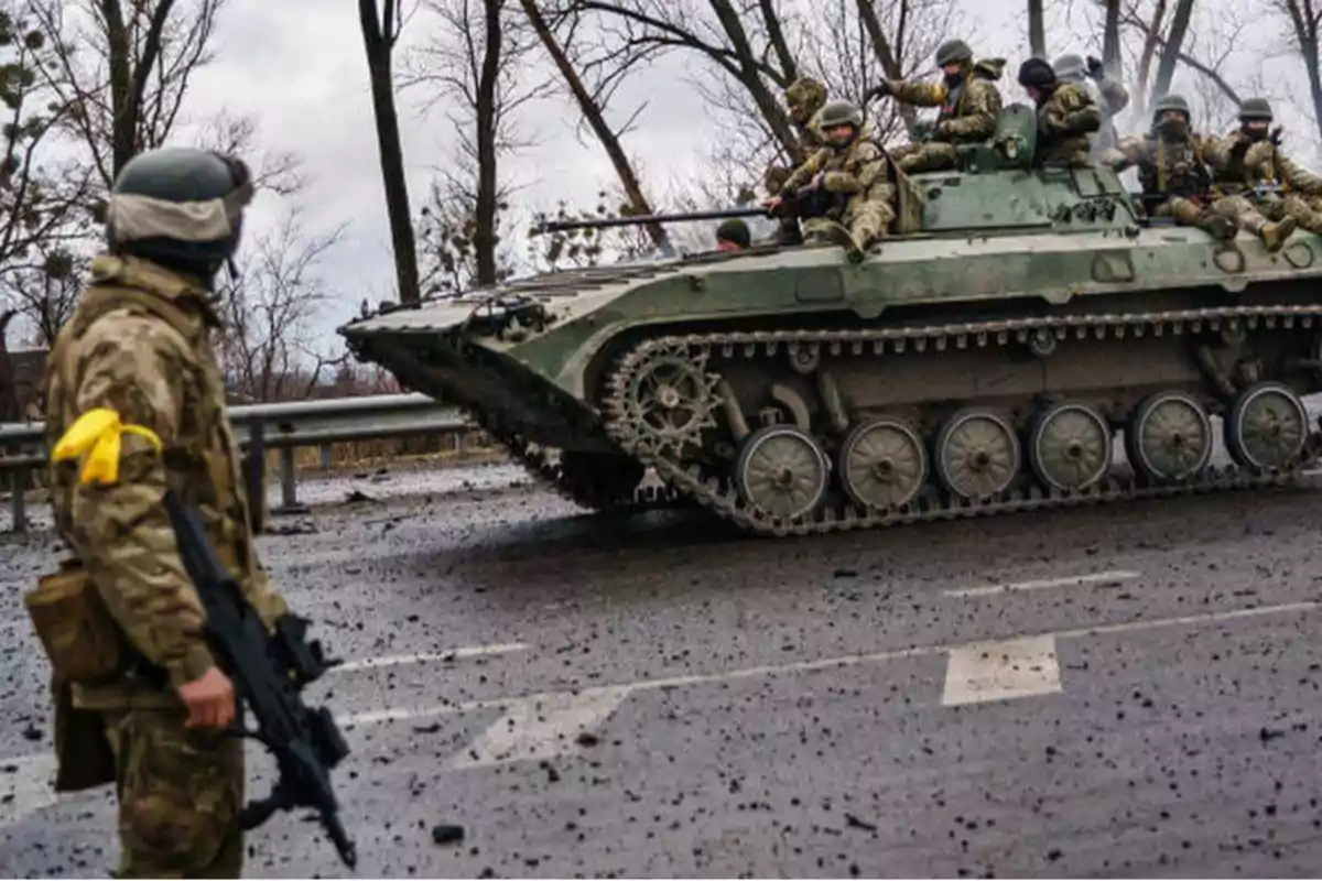 Soldados en uniforme militar junto a un vehículo blindado en una carretera.