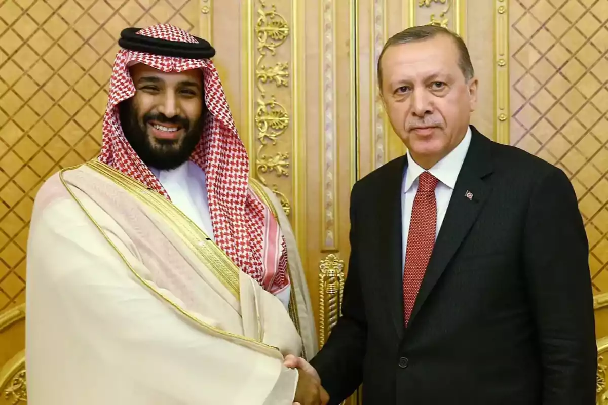 Dos hombres de pie estrechándose la mano frente a un fondo decorativo dorado. Dos hombres de pie estrechándose la mano frente a un fondo decorativo dorado.