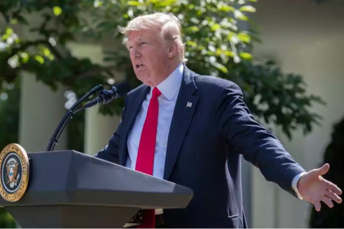 A man in a suit and red tie speaking at an outdoor podium.