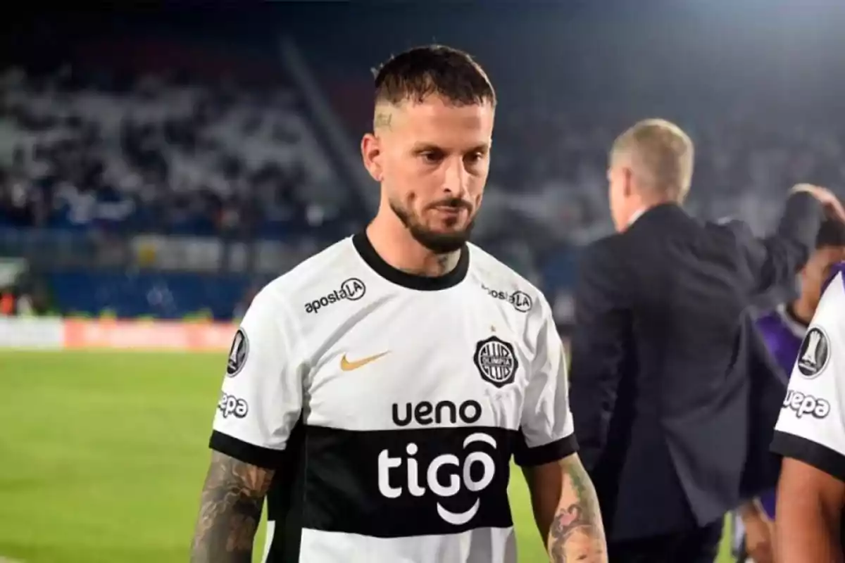 Un jugador de fútbol con uniforme blanco y negro camina en el campo de juego. Un jugador de fútbol con uniforme blanco y negro camina en el campo de juego.