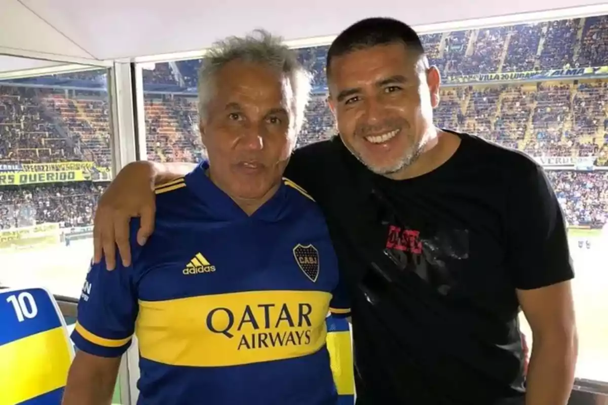 Two people smile while posing together in a soccer stadium, one of them wearing a Boca Juniors jersey. Two people smile while posing together in a soccer stadium, one of them wearing a Boca Juniors jersey.