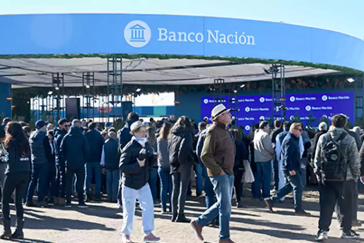 Personas reunidas frente a un stand de Banco Nación en un evento al aire libre durante el día Personas reunidas frente a un stand de Banco Nación en un evento al aire libre durante el día