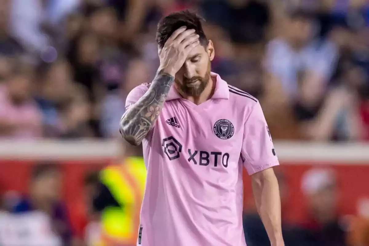 Un jugador de fútbol con uniforme rosa se lleva la mano a la cabeza en un campo de juego.