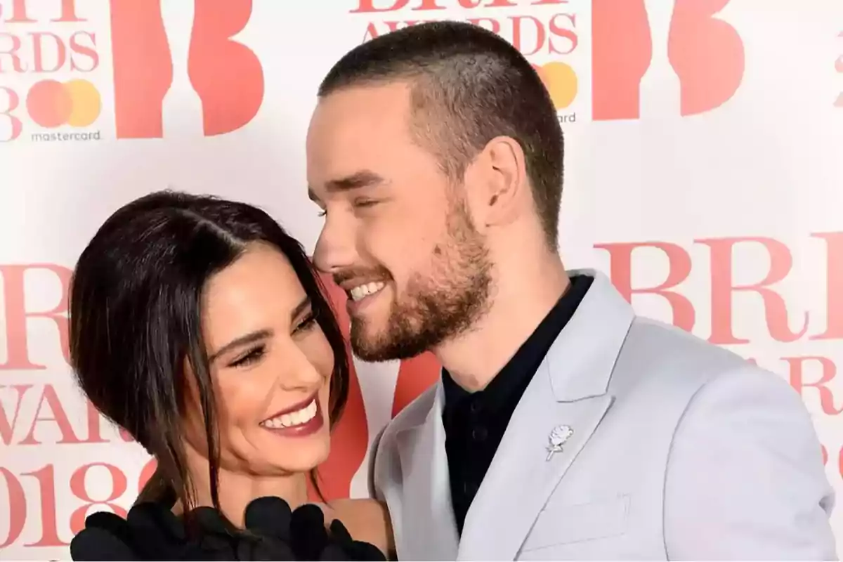 Una pareja sonriente posando en un evento de premios con fondo de logotipos.