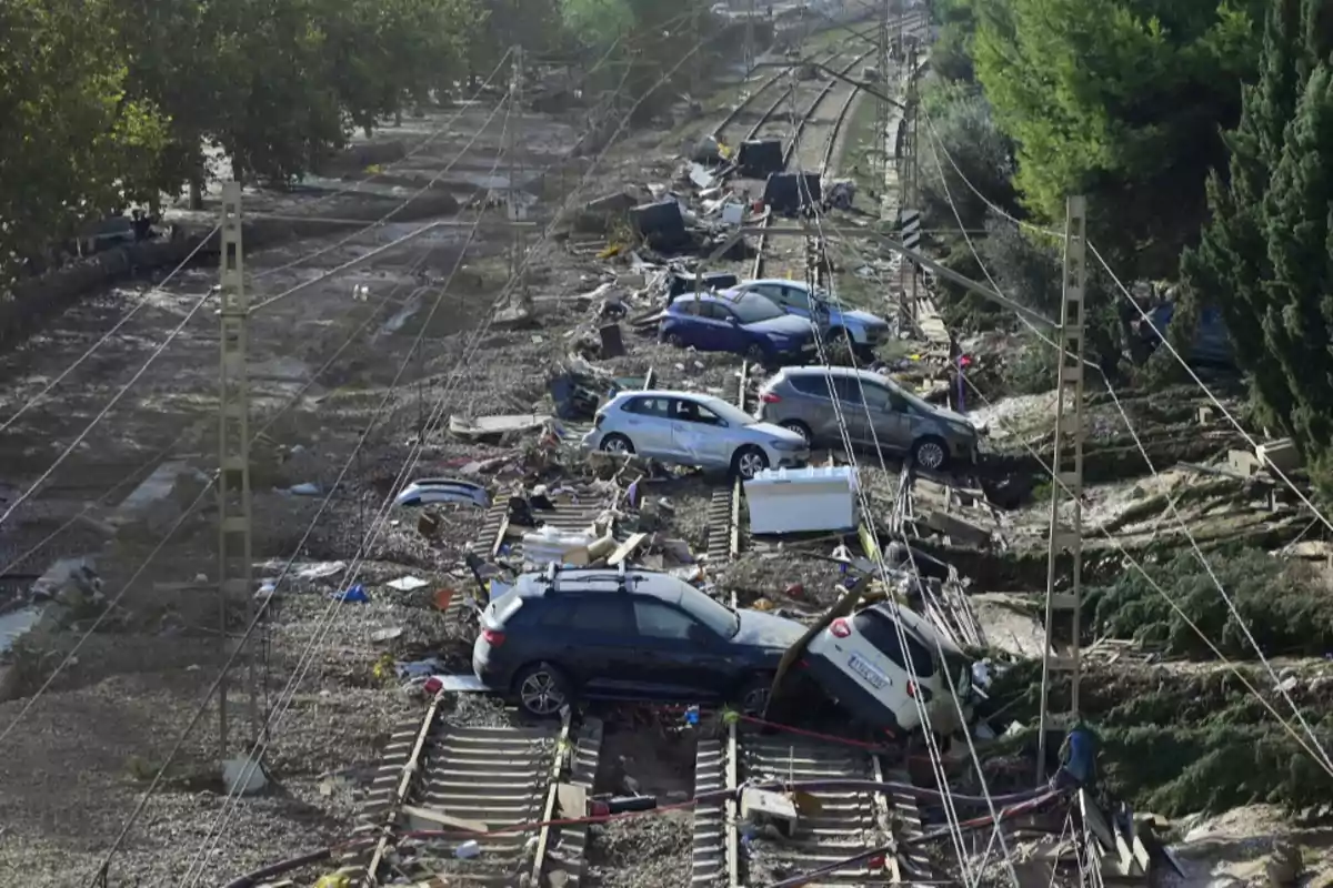 Coches y escombros sobre vías de tren tras una inundación.