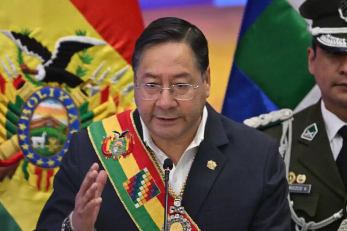 Man wearing the presidential sash of Bolivia speaking in front of a microphone with flags in the background