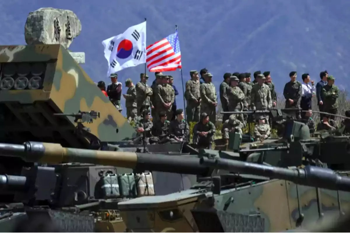 Soldados en uniforme militar junto a tanques y banderas de Corea del Sur y Estados Unidos en un entorno montañoso.