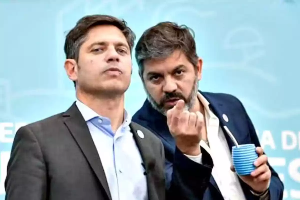 Dos hombres en traje, uno de ellos sosteniendo un mate, posan frente a un fondo azul.