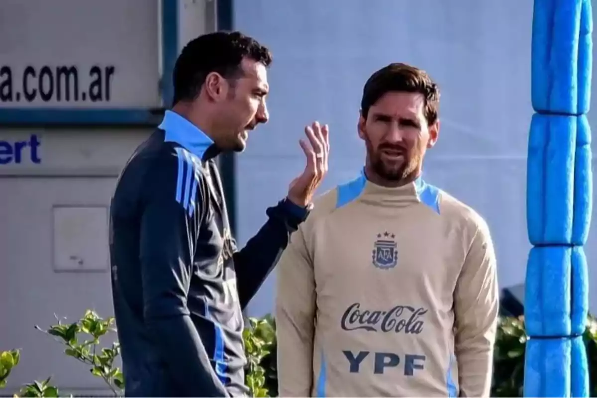 Two men wearing Argentina national team sportswear are talking on a training field.