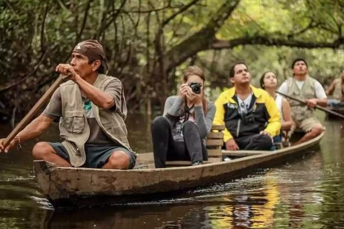 Un grupo de personas navega en una canoa por un río rodeado de vegetación densa, mientras una de ellas toma fotografías.