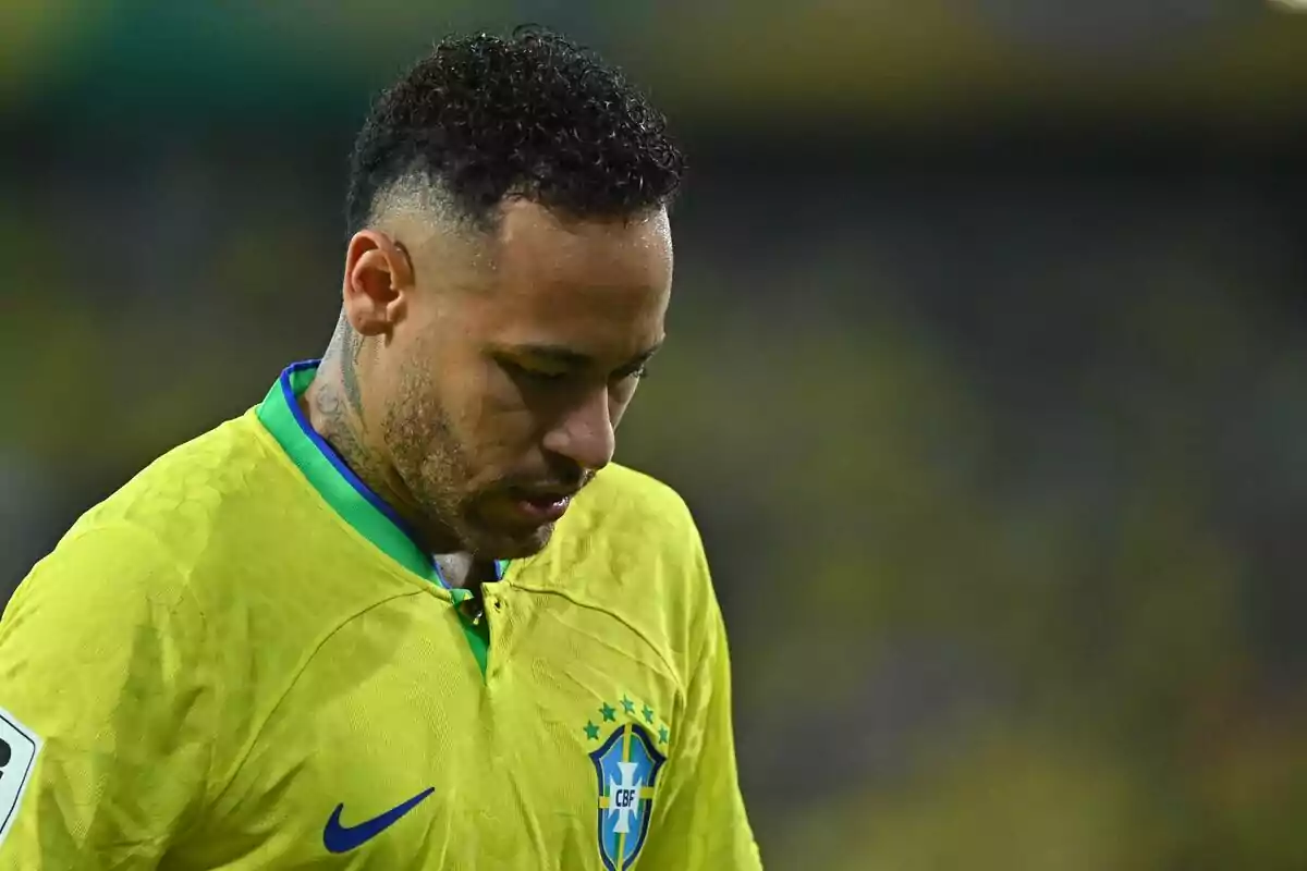 Un jugador de fútbol con la camiseta amarilla de Brasil mira hacia abajo en el campo.