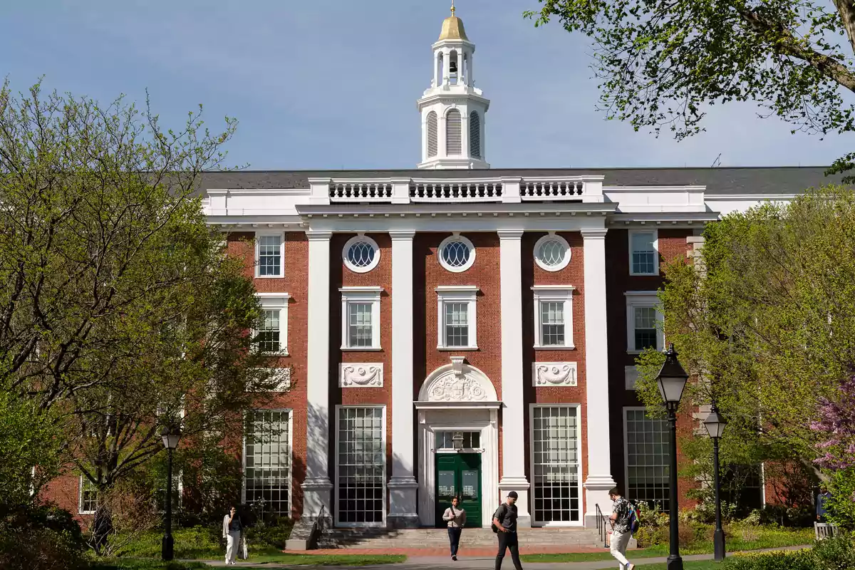 Red brick building with white columns and a golden dome on top, surrounded by trees and people walking in the front. Red brick building with white columns and a golden dome on top, surrounded by trees and people walking in the front.