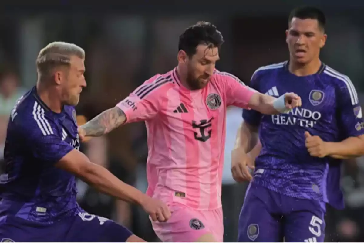 Soccer players competing for the ball in a match, one of them wearing a pink uniform and the other two dressed in purple. Soccer players competing for the ball in a match, one of them wearing a pink uniform and the other two dressed in purple.