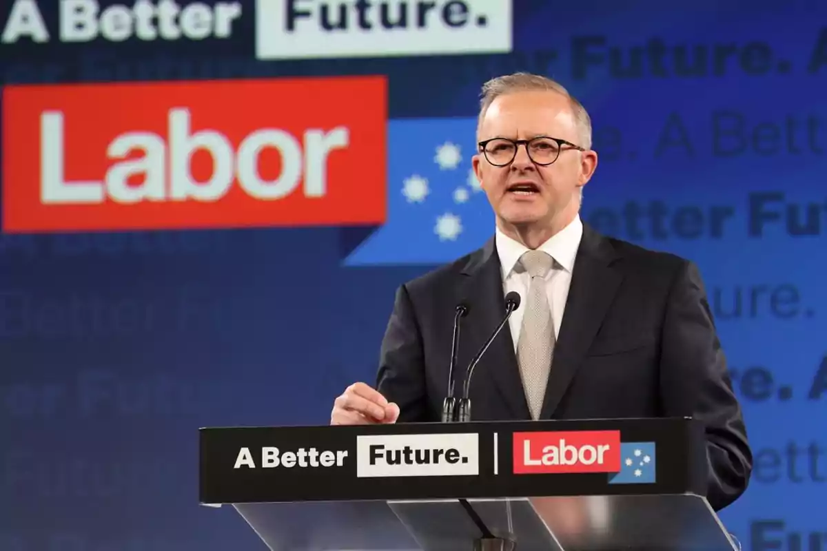 A man with glasses and a suit speaks at a podium with the logos A man with glasses and a suit speaks at a podium with the logos