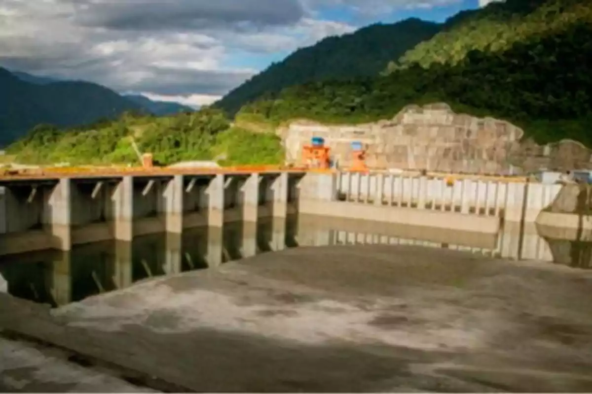 Una represa rodeada de montañas y vegetación bajo un cielo nublado.