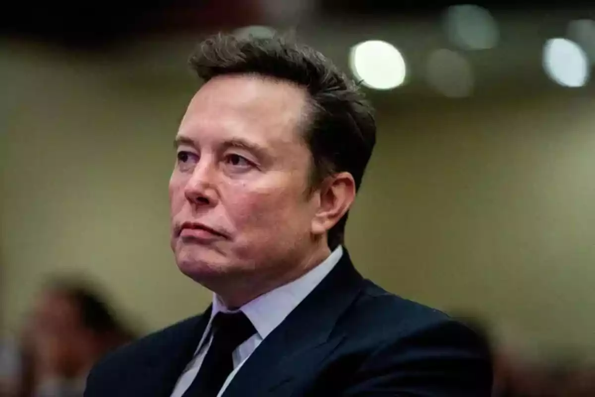 A man in a dark suit with a serious expression in an indoor setting.