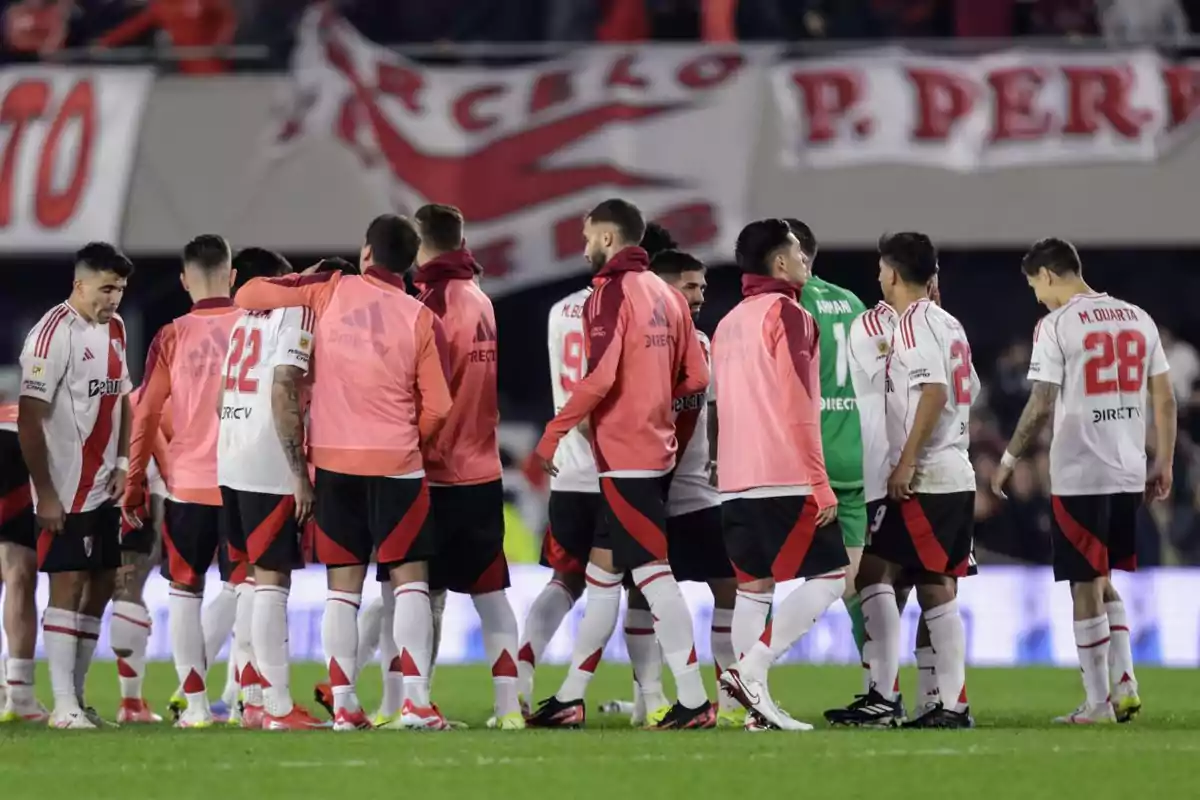 A group of players in white and red uniforms gathers on the field, some wearing pink vests, while a banner is visible in the background. A group of players in white and red uniforms gathers on the field, some wearing pink vests, while a banner is visible in the background.