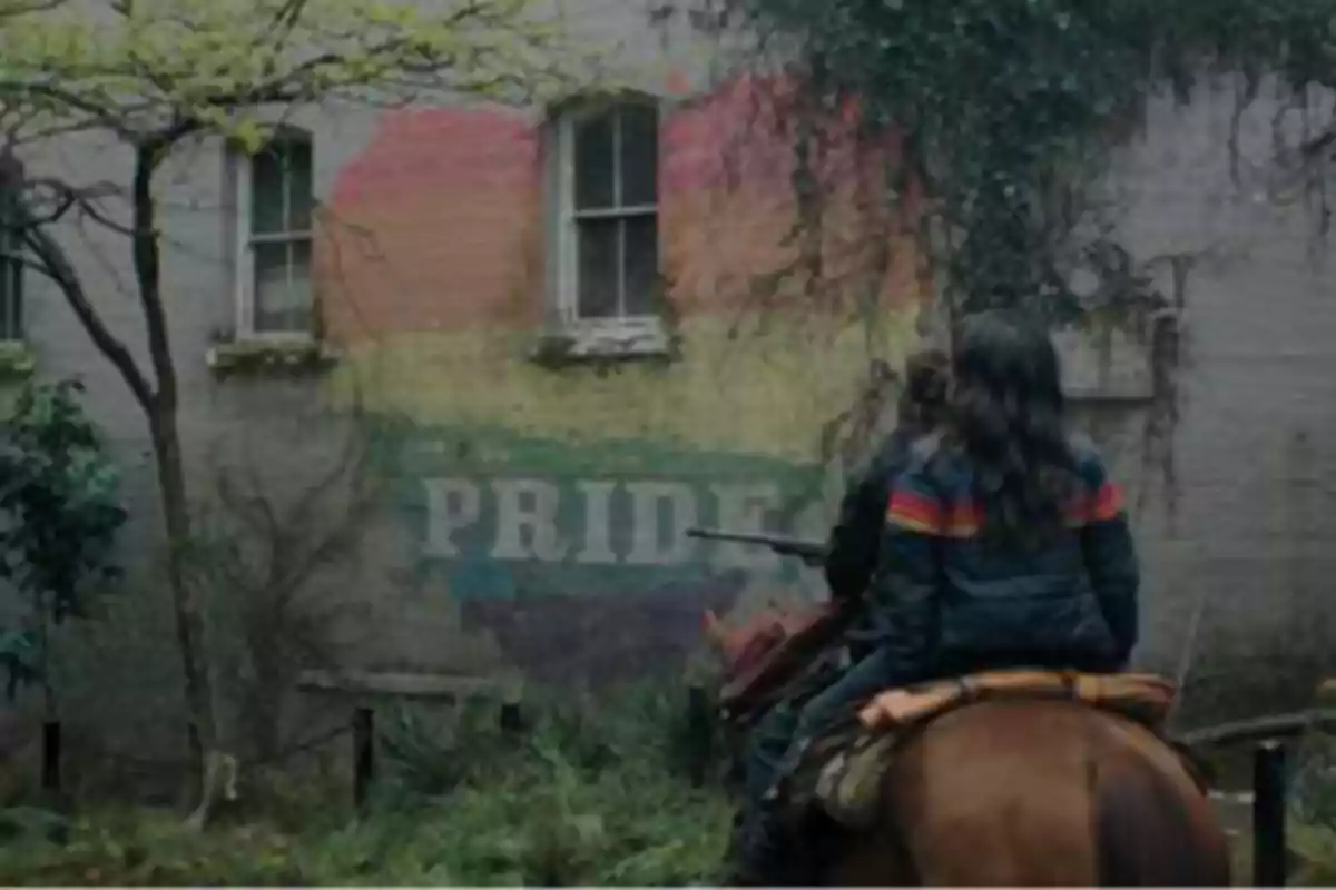 Person riding a horse observes a mural with the rainbow flag and the word PRIDE on a wall covered in vegetation. Person riding a horse observes a mural with the rainbow flag and the word PRIDE on a wall covered in vegetation.