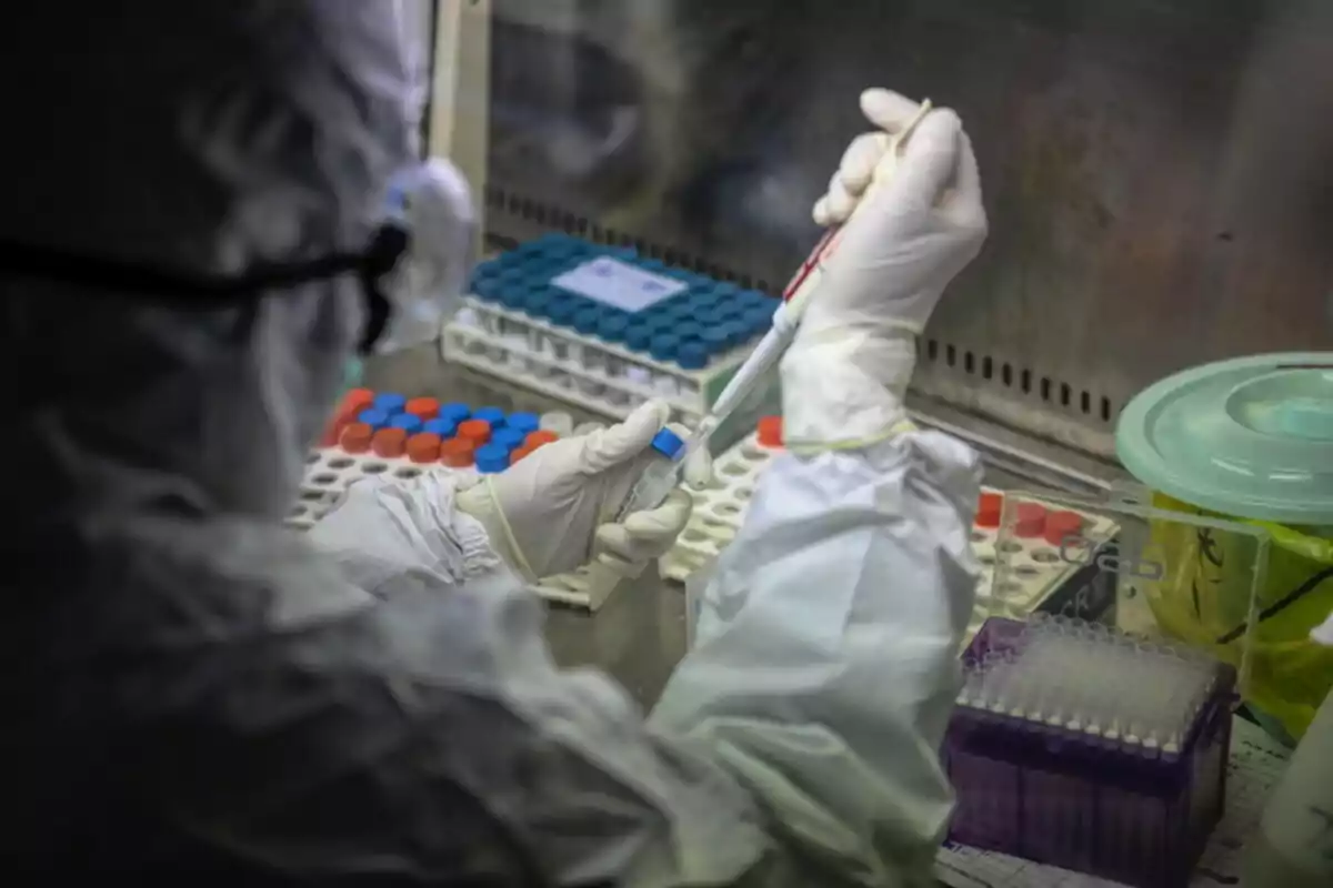 Persona con traje de protección manipulando muestras en un laboratorio.