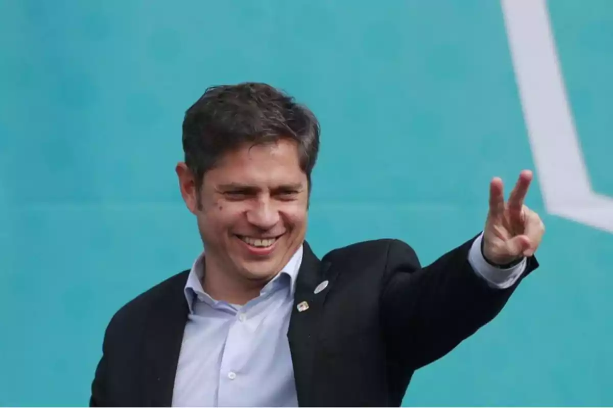 Un hombre sonriendo hace un gesto de paz con la mano frente a un fondo azul.