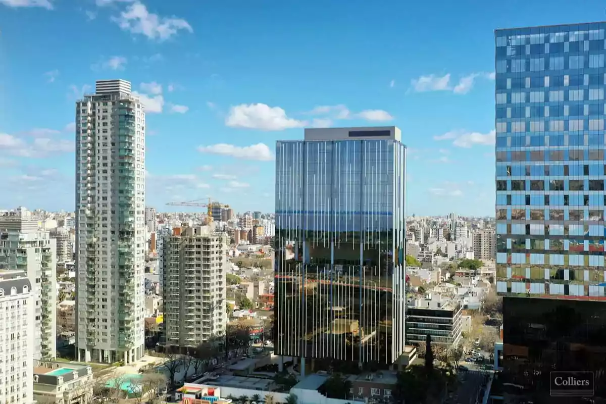Vista de una ciudad con varios edificios altos y modernos bajo un cielo azul con algunas nubes.