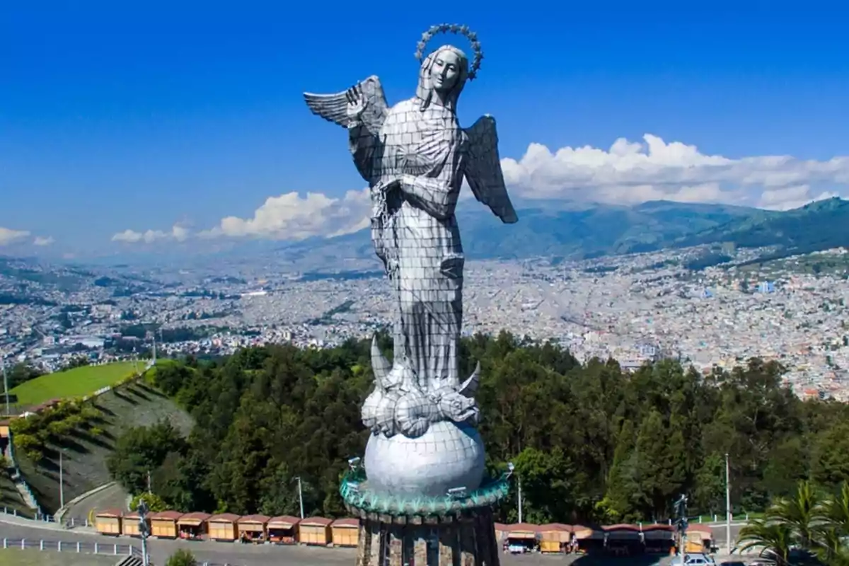 Statue of an angel on a hill with a city and mountains in the background.