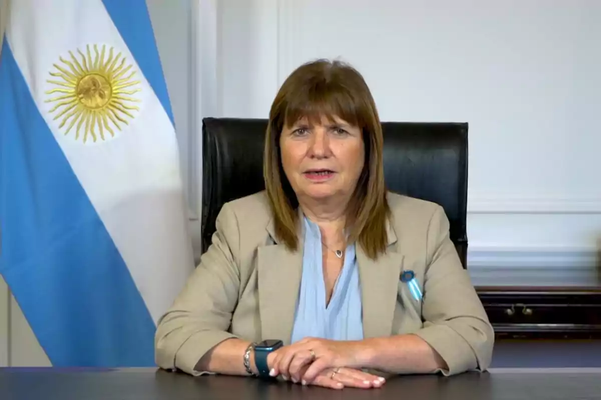 A woman sitting at a desk with an Argentine flag in the background.