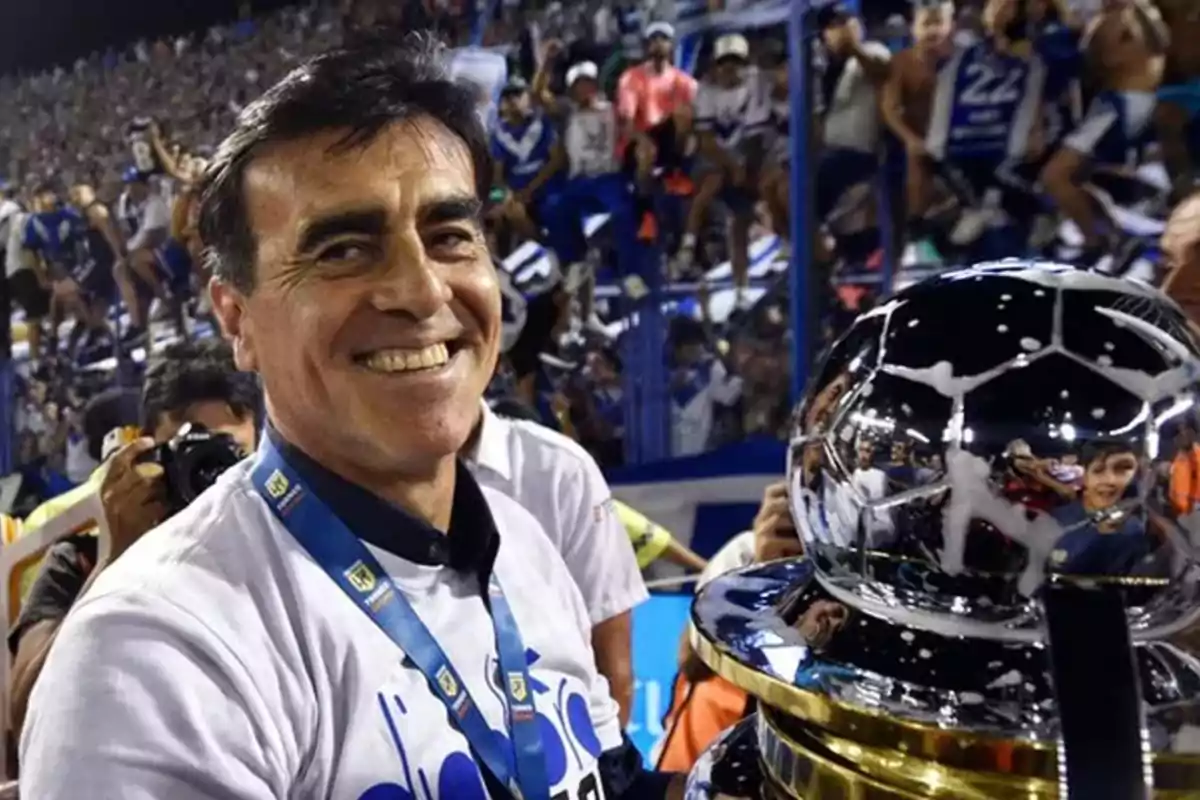 Hombre sonriente con medalla y trofeo en un estadio lleno de aficionados.