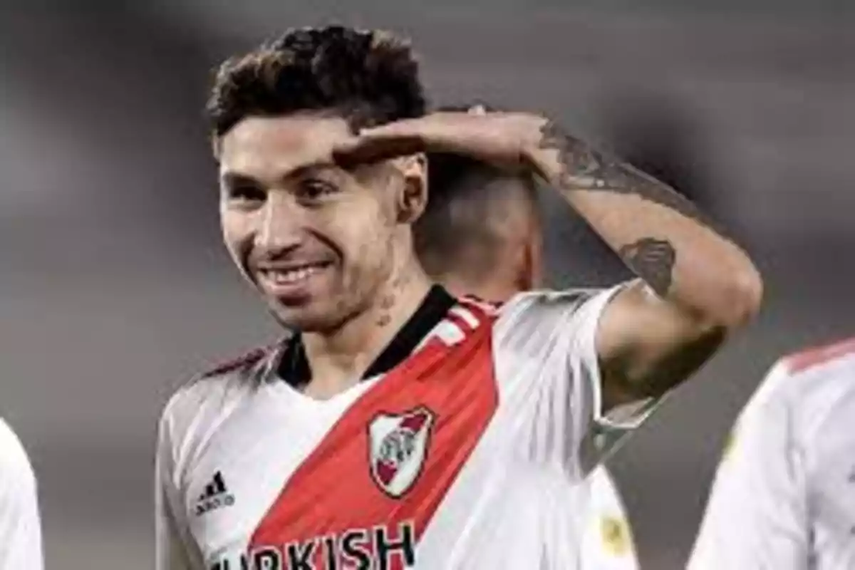 Jugador de fútbol con uniforme blanco y rojo haciendo un gesto de saludo con la mano en la frente.