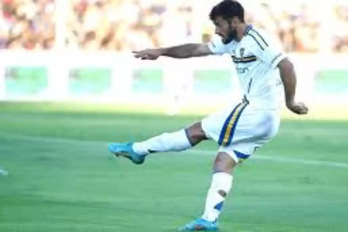 Un jugador de fútbol con uniforme blanco y azul patea el balón en un campo de juego.