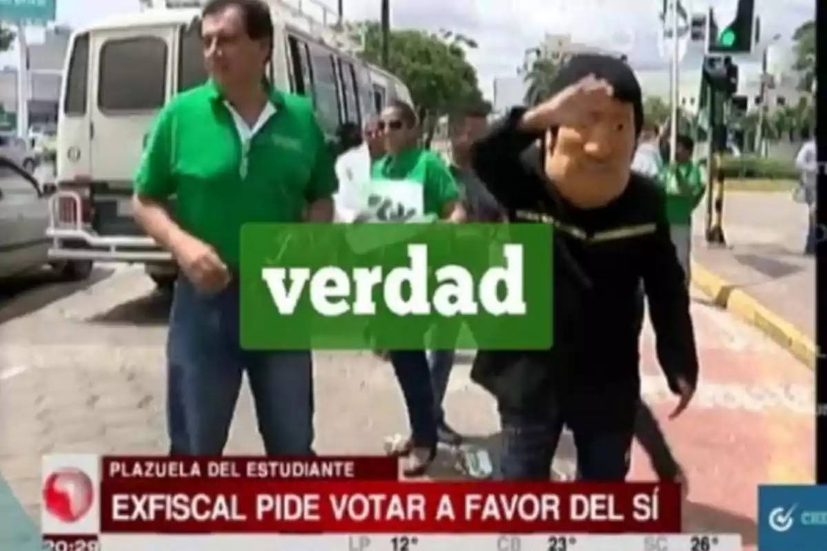 Un grupo de personas vestidas de verde camina por la calle, una de ellas lleva una máscara grande y saluda, mientras un texto en la pantalla dice 