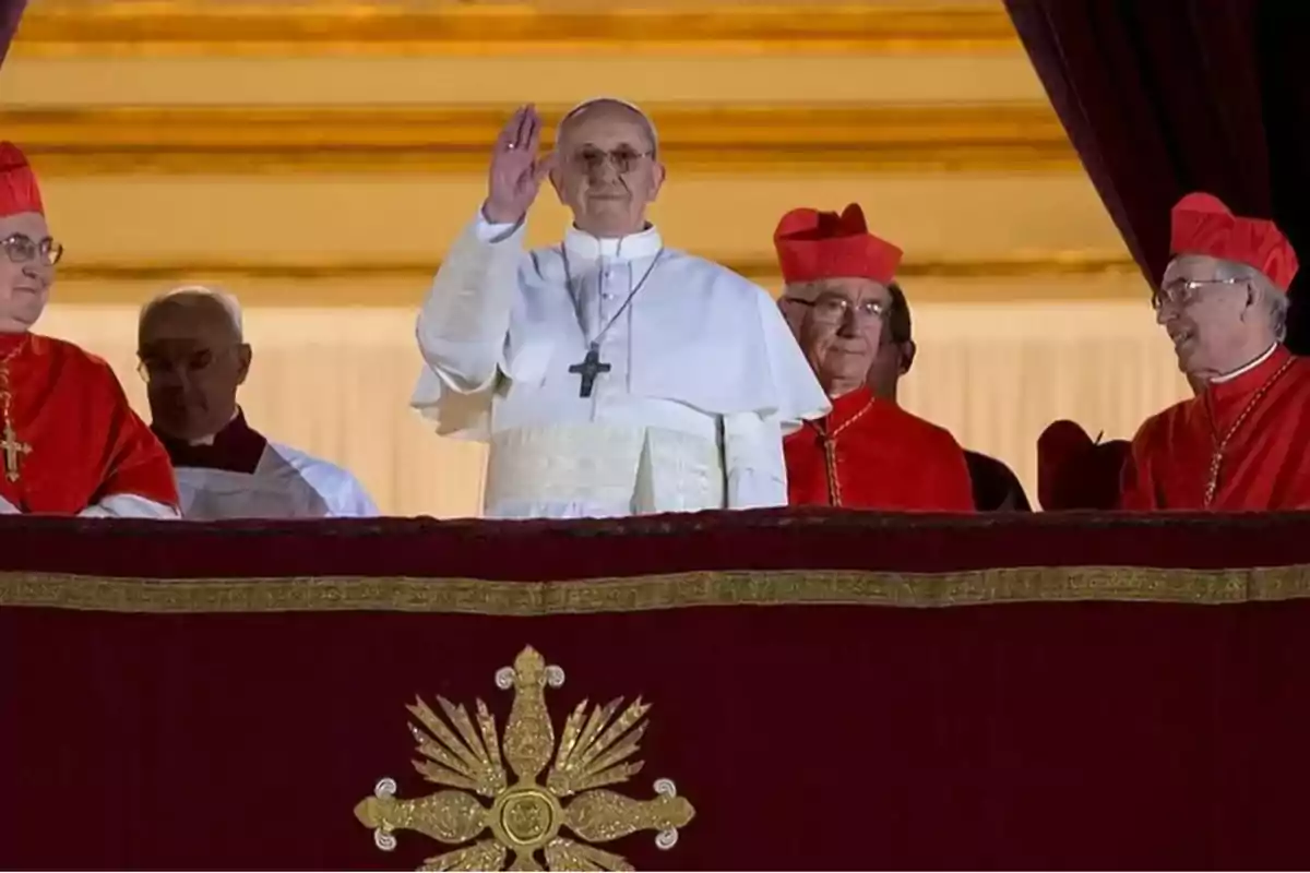 Un líder religioso vestido de blanco saluda desde un balcón acompañado de varios cardenales con vestimentas rojas. Un líder religioso vestido de blanco saluda desde un balcón acompañado de varios cardenales con vestimentas rojas.