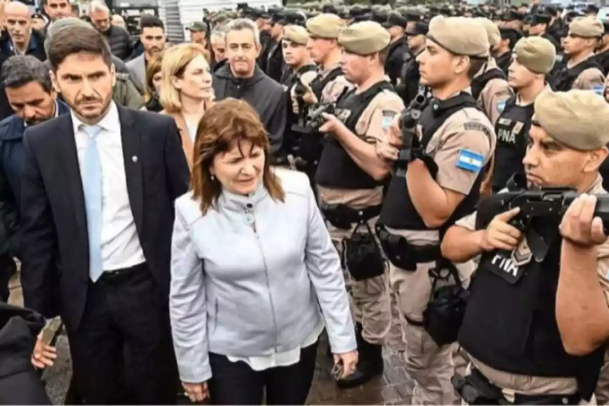 A group of people walks between a row of uniformed officers holding weapons, while others watch in the background.