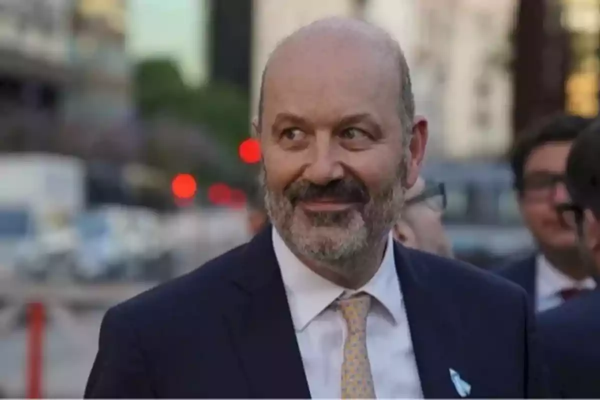 Hombre de mediana edad con barba y traje sonríe mientras está al aire libre en una ciudad