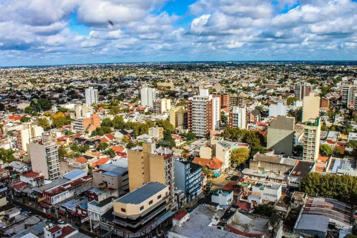 Panoramic view of a city with tall buildings, houses, and trees under a partly cloudy sky