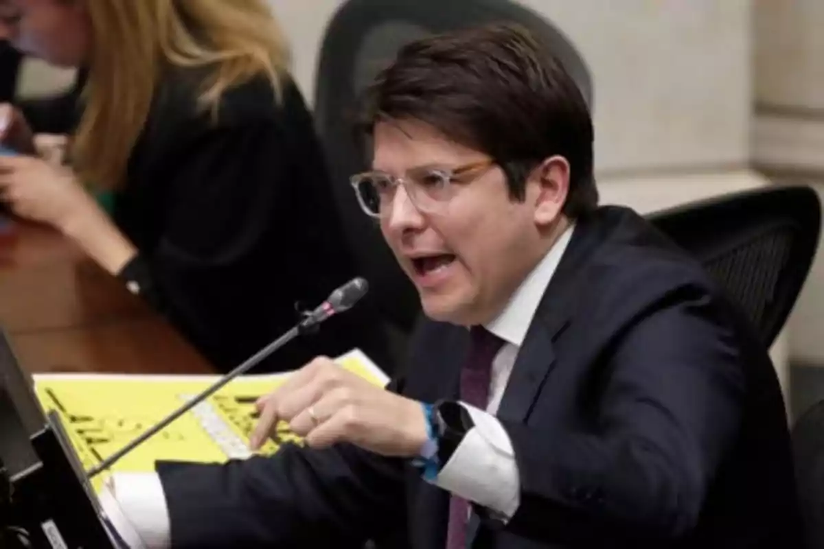 Man with glasses and a suit speaking into a microphone during a meeting or formal session