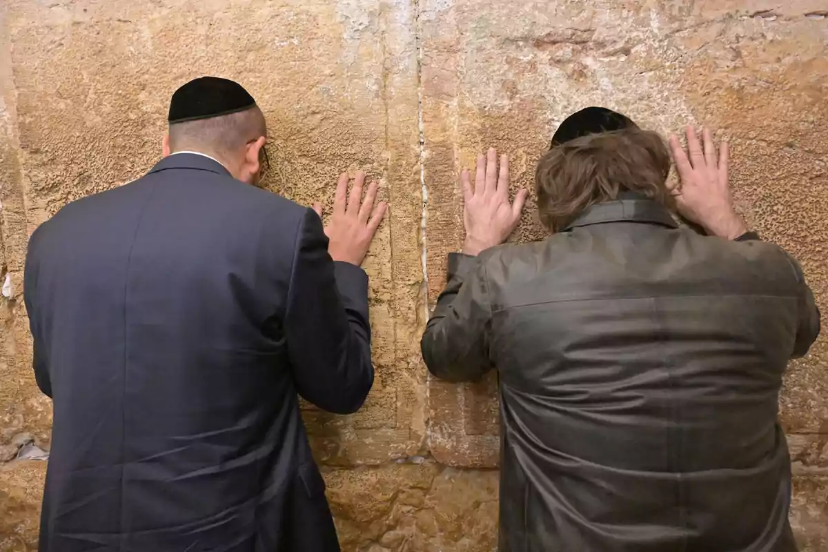 Dos hombres rezan de espaldas tocando el Muro de los Lamentos con las manos apoyadas en la piedra