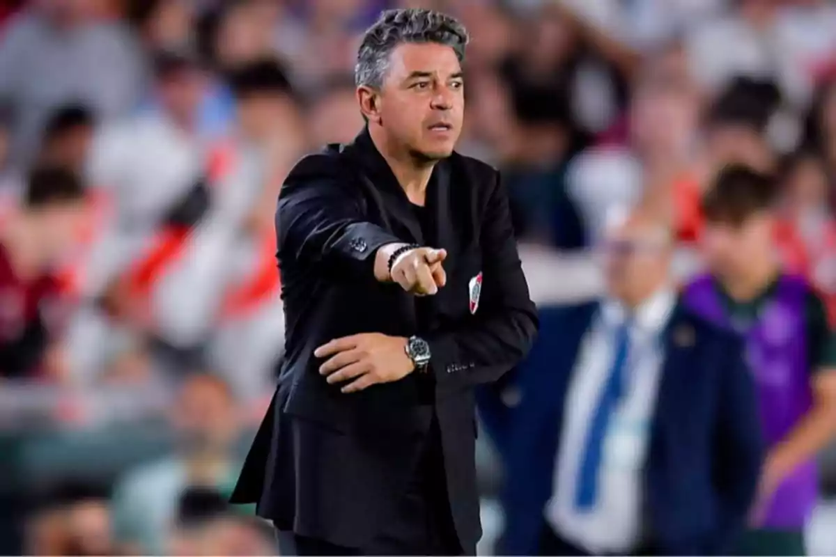 Soccer coach in a black suit giving instructions during a match with a crowd in the background