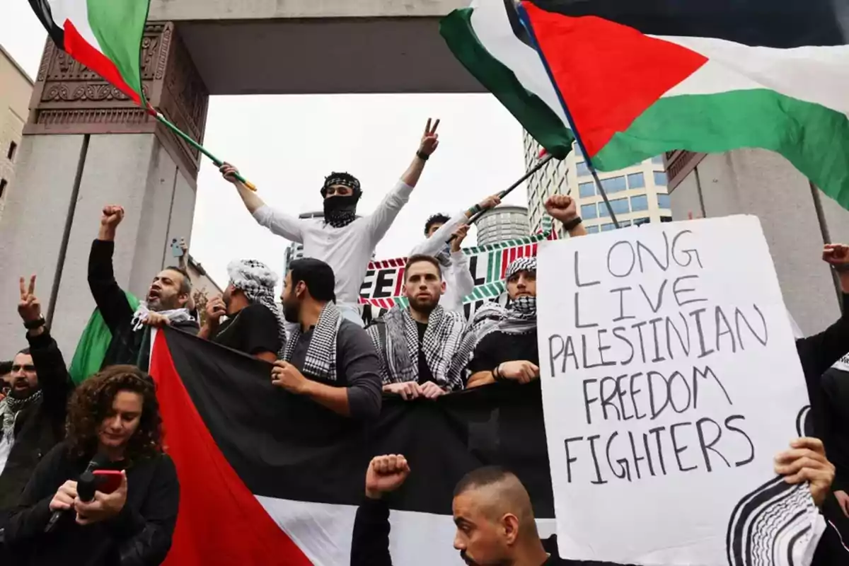 Grupo de personas en una manifestación sosteniendo banderas palestinas y un cartel que apoya a los luchadores por la libertad de Palestina.