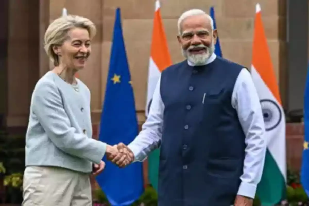 Dos personas dándose la mano frente a banderas de la Unión Europea e India. Dos personas dándose la mano frente a banderas de la Unión Europea e India.