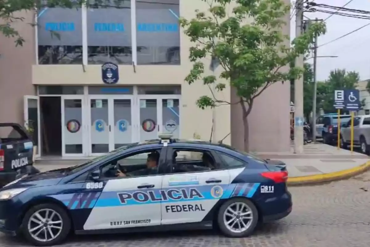 Un patrullero de la Policía Federal Argentina estacionado frente a un edificio policial en una calle con árboles y señalización para personas con discapacidad
