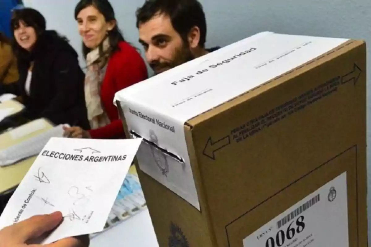 A person is inserting an envelope into a ballot box during the elections in Argentina, while three people watch from a table. A person is inserting an envelope into a ballot box during the elections in Argentina, while three people watch from a table.
