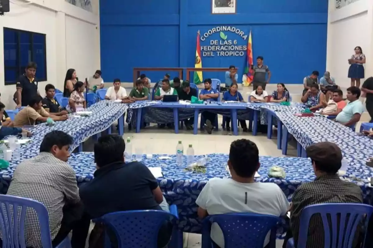People sitting around U-shaped tables in a blue room during a meeting of the Coordinator of the 6 Federations of the Tropic People sitting around U-shaped tables in a blue room during a meeting of the Coordinator of the 6 Federations of the Tropic