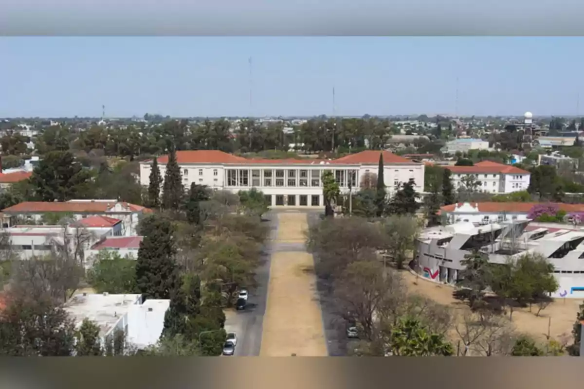 Vista aérea de un campus universitario con edificios de techos rojos rodeados de árboles y una avenida central que conduce a un edificio principal Vista aérea de un campus universitario con edificios de techos rojos rodeados de árboles y una avenida central que conduce a un edificio principal