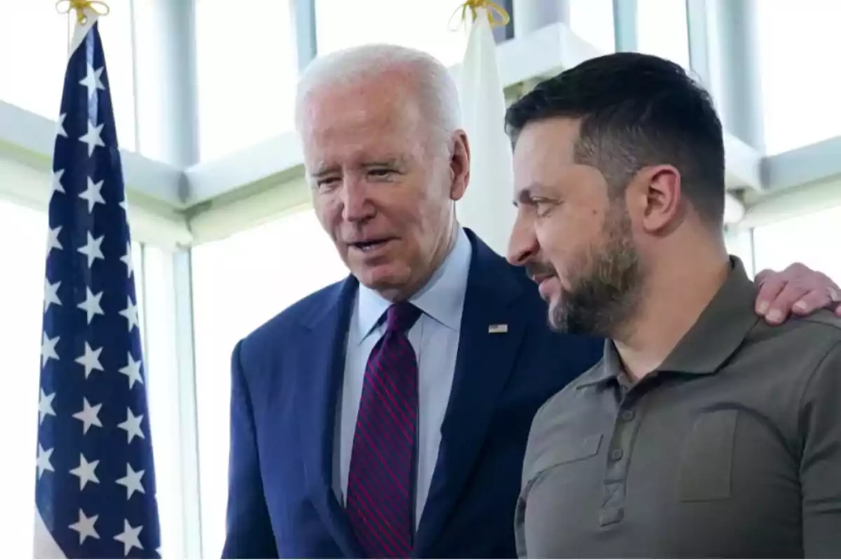 Dos hombres conversando amistosamente junto a una bandera de Estados Unidos.