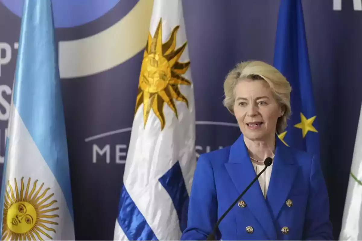 Mujer hablando frente a banderas de Argentina, Uruguay y la Unión Europea.