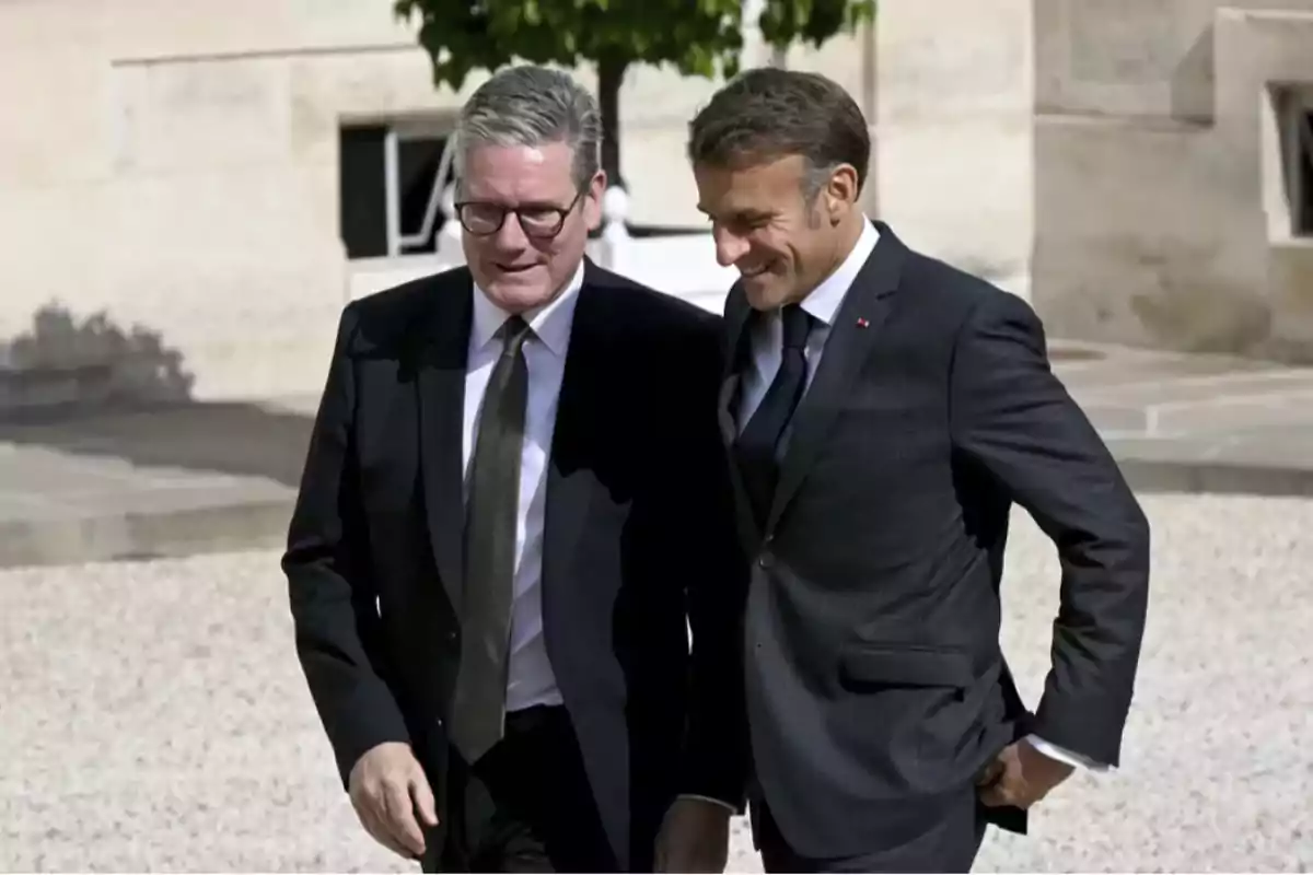 Two men in dark suits walking together and smiling in an outdoor setting.