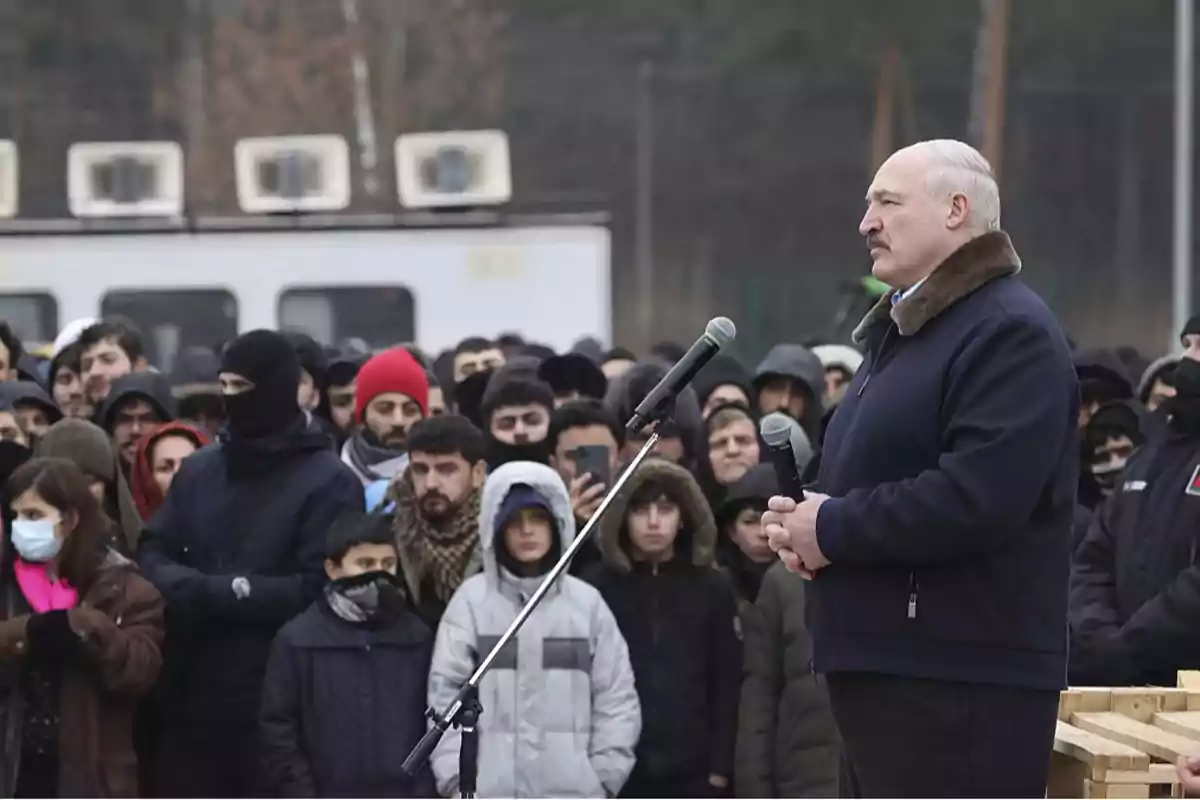 Un hombre de pie frente a un micrófono se dirige a una multitud de personas abrigadas en un entorno al aire libre.