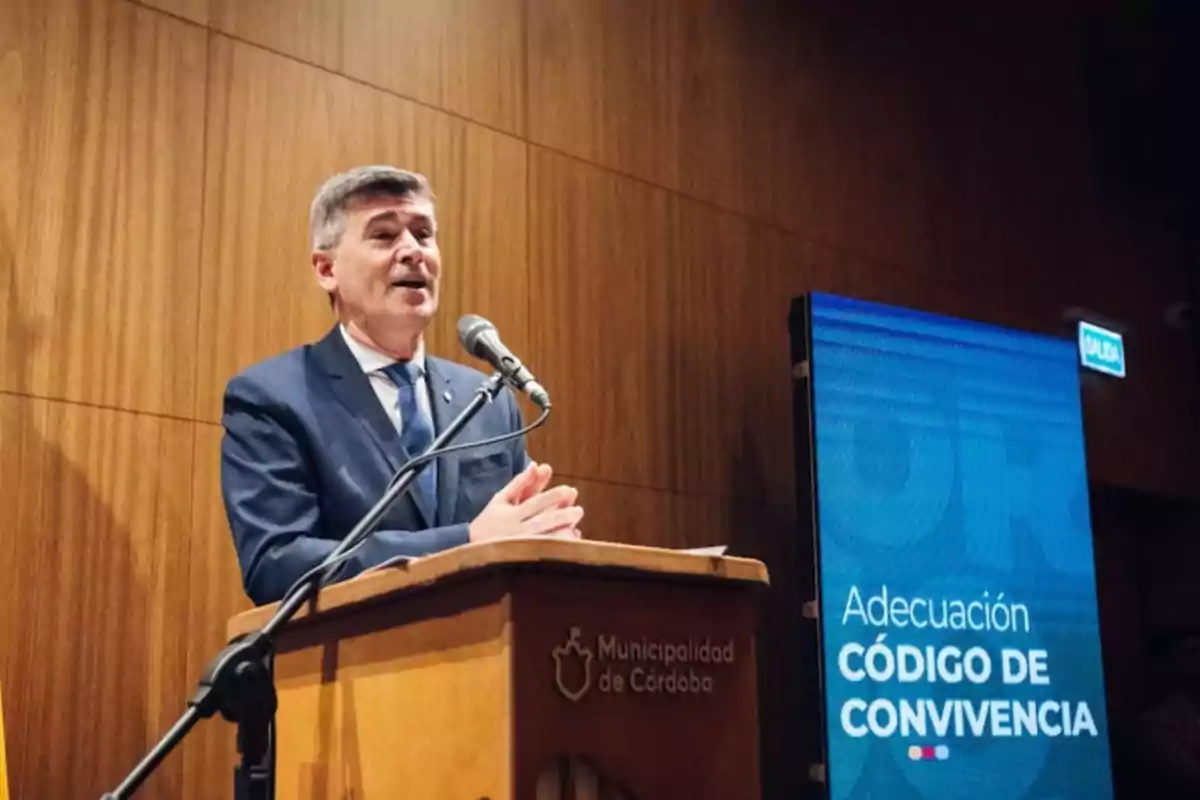 A man in a suit speaks at a podium with the logo of the Municipality of Córdoba while next to him there is a blue screen that says Adjustment of the Code of Coexistence. A man in a suit speaks at a podium with the logo of the Municipality of Córdoba while next to him there is a blue screen that says Adjustment of the Code of Coexistence.