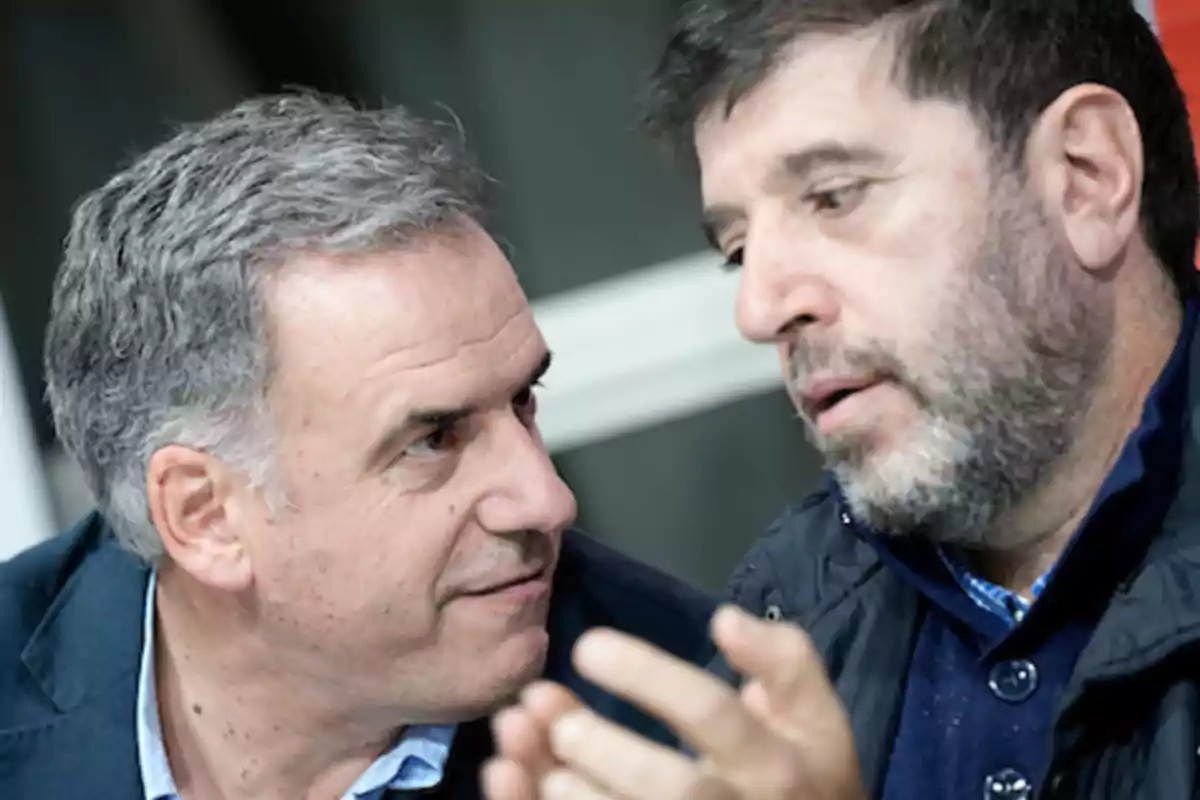 Two men talking closely, one of them gesturing with his hand. Two men talking closely, one of them gesturing with his hand.